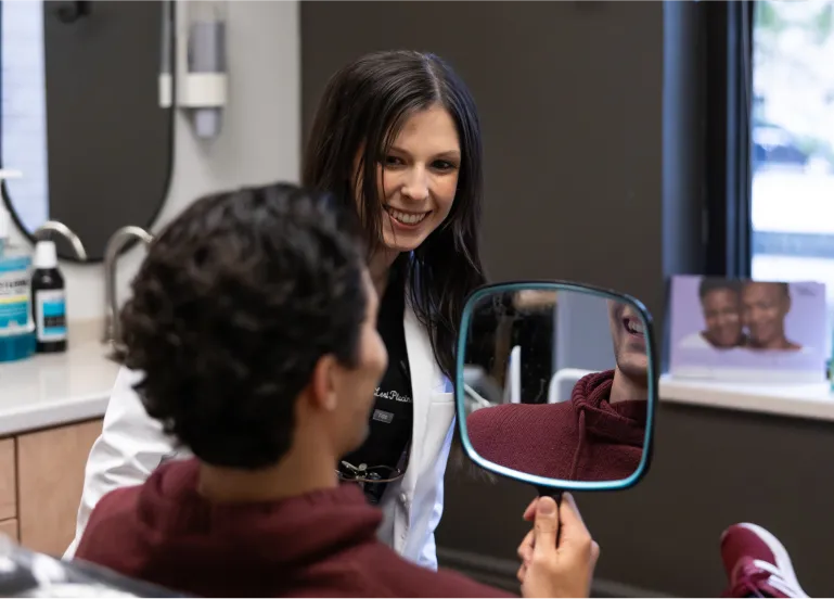 Doctor watching patient look at his teeth in a mirror while smiling